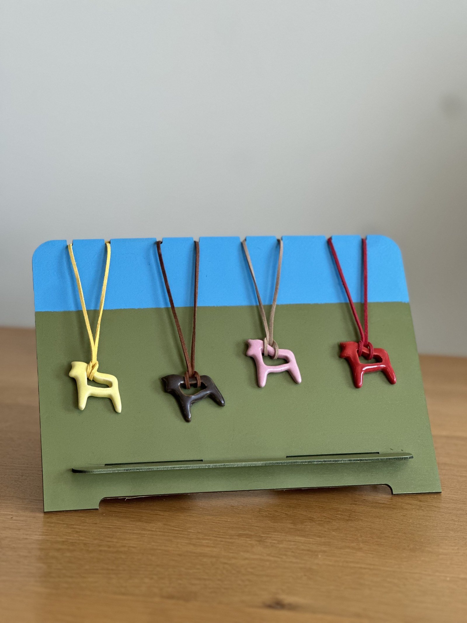 Four ceramic horse pendants in different colors displayed on a painted stand