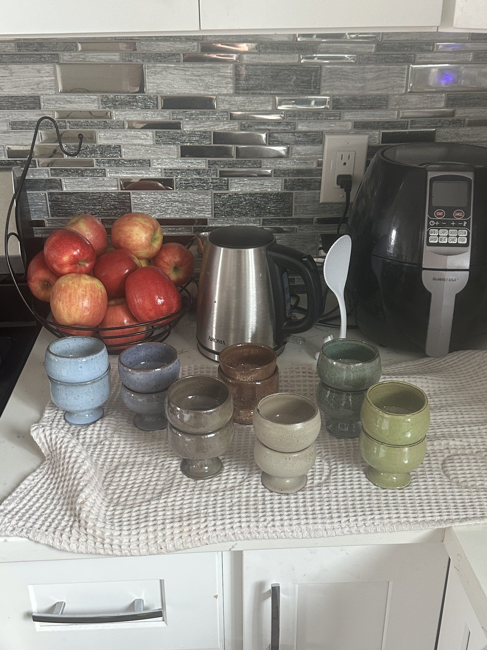 A kitchen counter filled with a growing collection of handmade ceramic cups and vessels