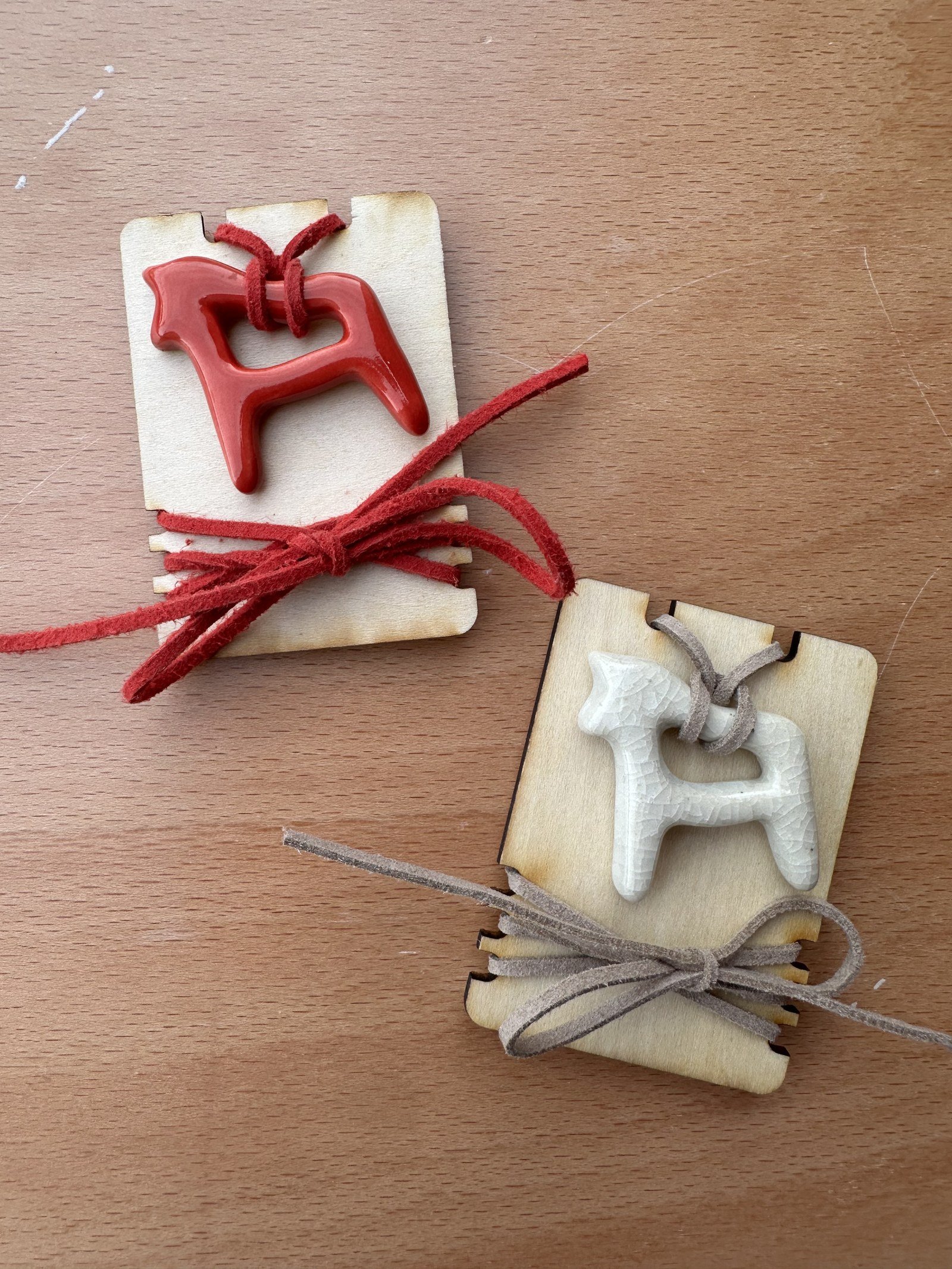 Two ceramic letter pendants with leather cord packaging on a wooden surface