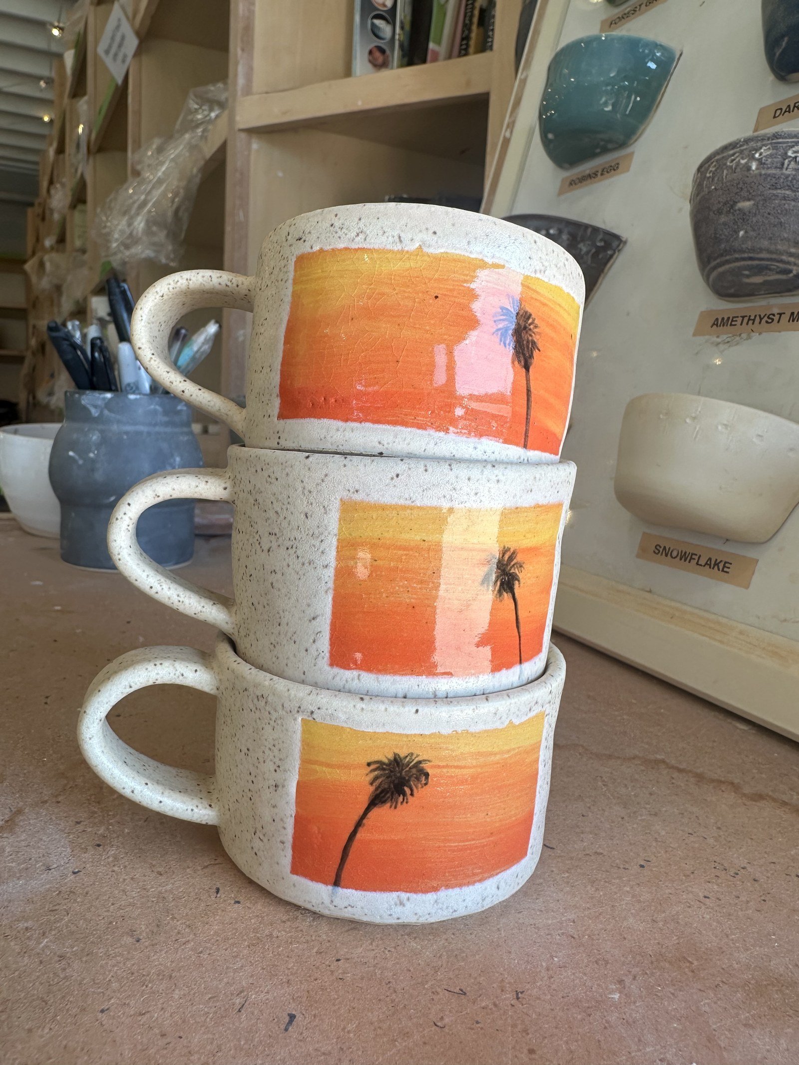 Three ceramic mugs with California sunset and palm tree paintings stacked together